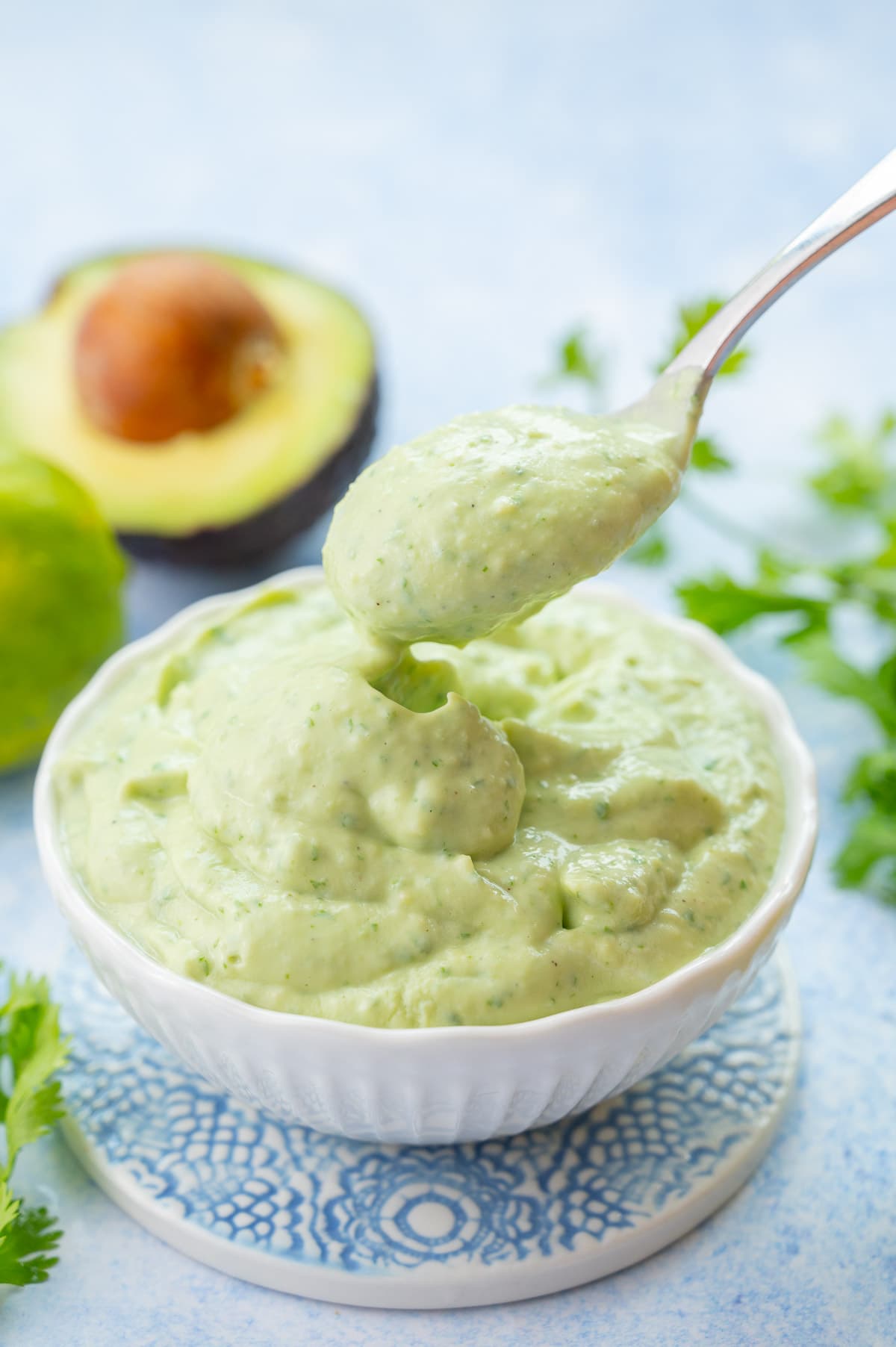 Avocado sauce in a white bowl on a blue background. The sauce is being scooped with a spoon.