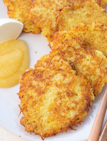 German potato pancakes served with sour cream and apple sauce on a beige plate.