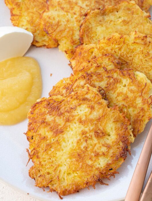 German potato pancakes served with sour cream and apple sauce on a beige plate.