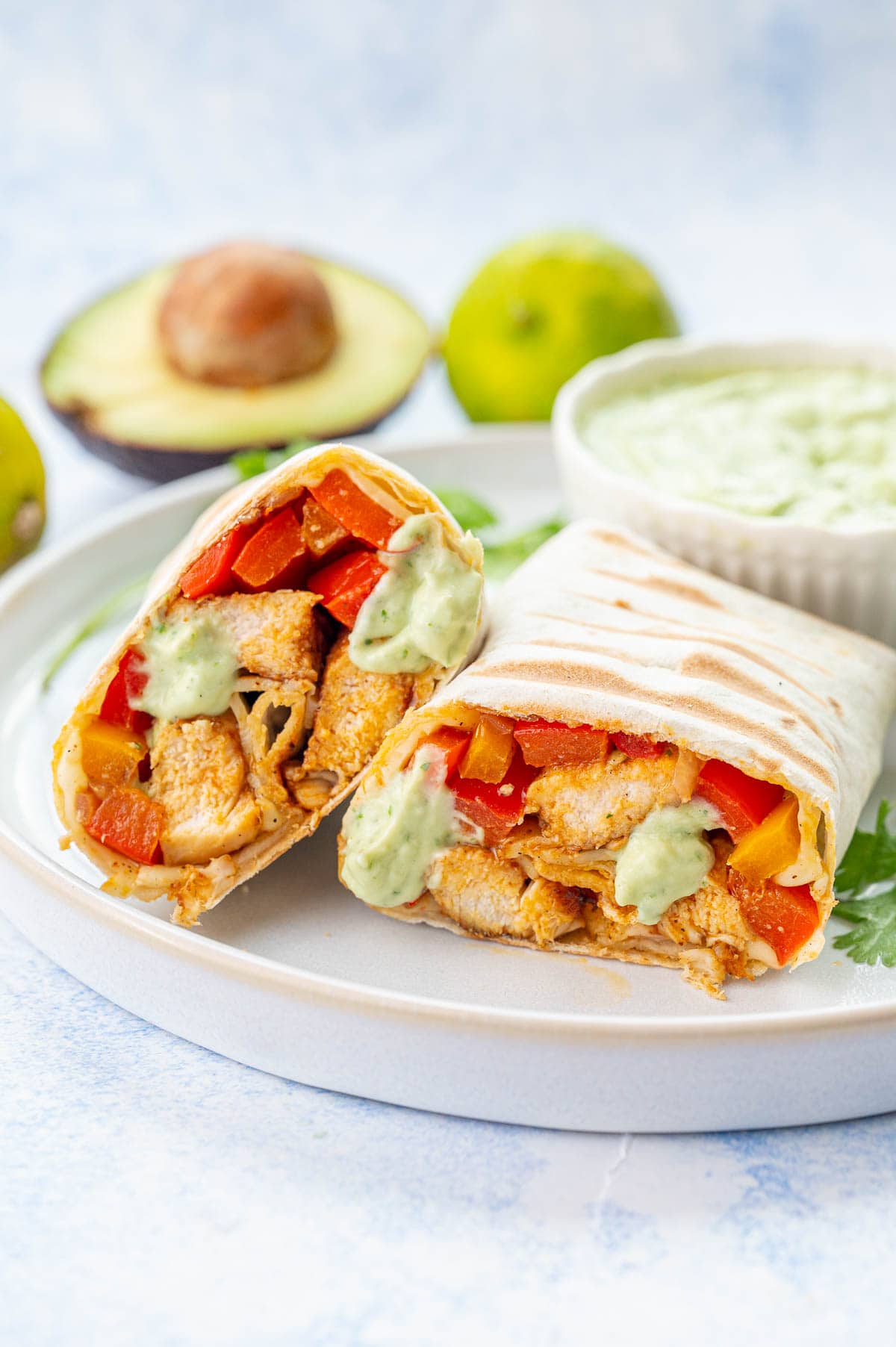 Chicken Fajita wraps cut in half on a white plate.