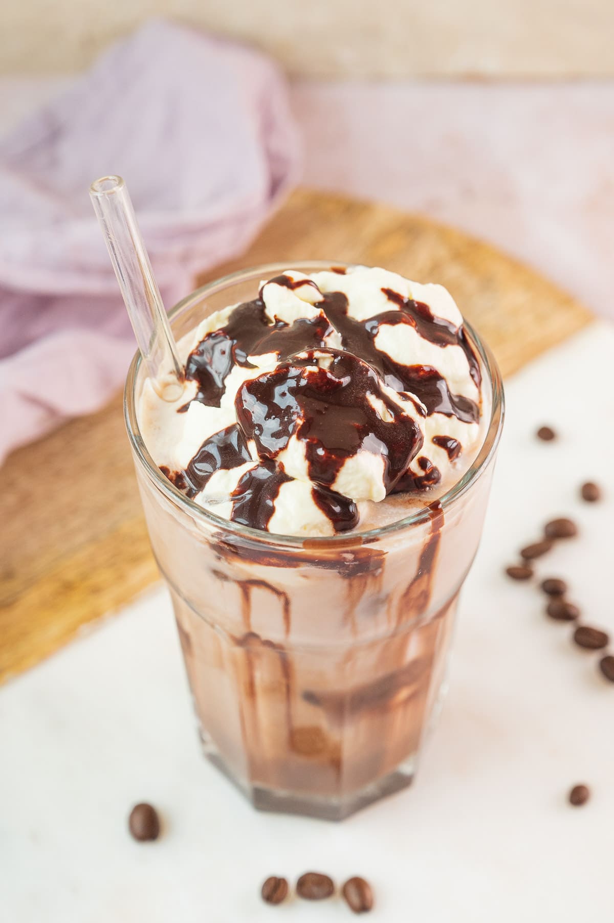 Iced mocha in a glass topped with whipped cream and chocolate syrup.