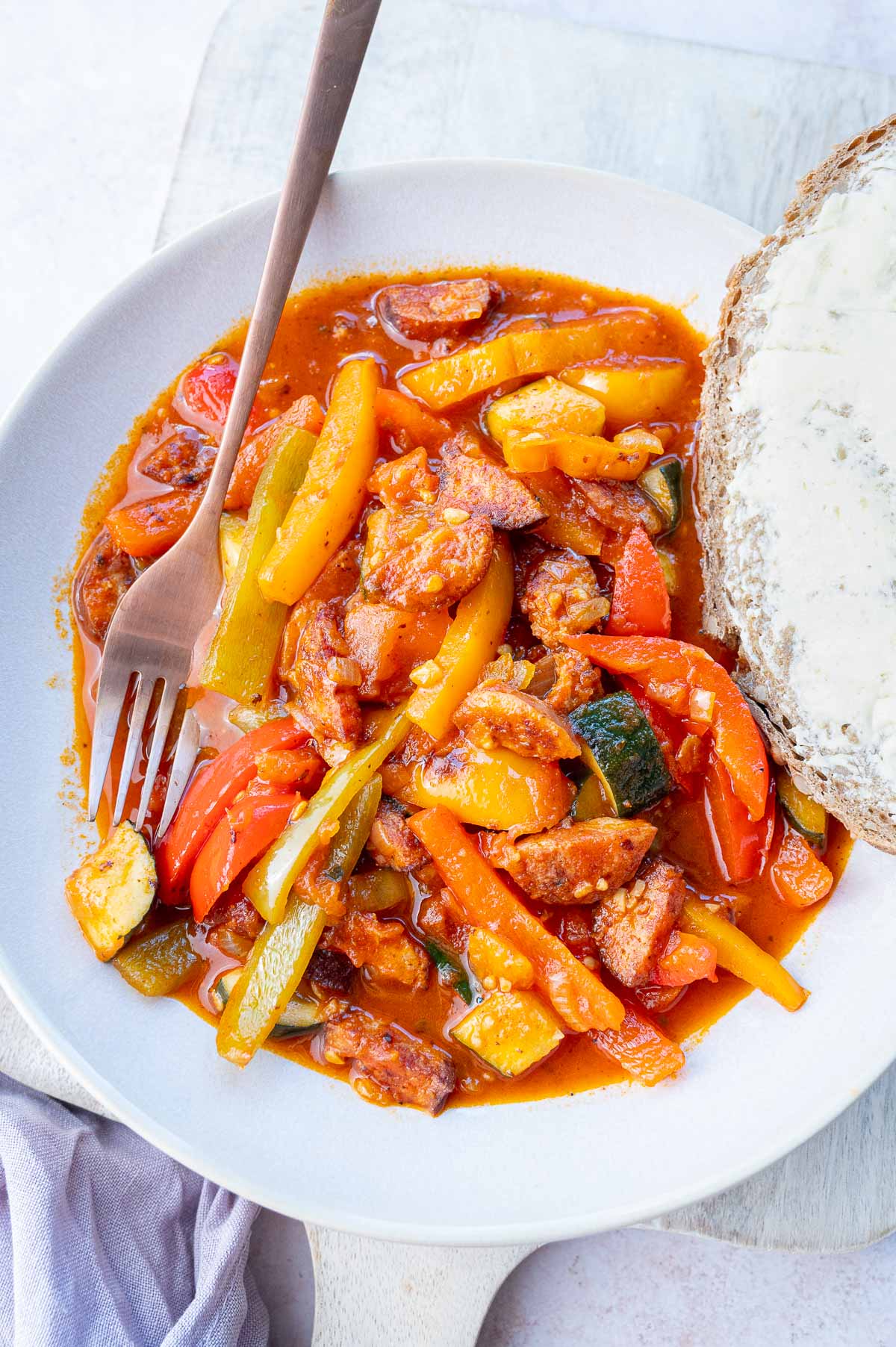 Polish leczo stew in a white plate with a fork and a piece of bread on the side.