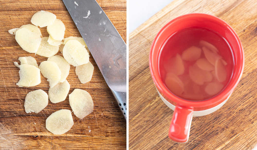 Sliced ginger on a chopping board. Ginger is steeping in boiling water in a red cup.