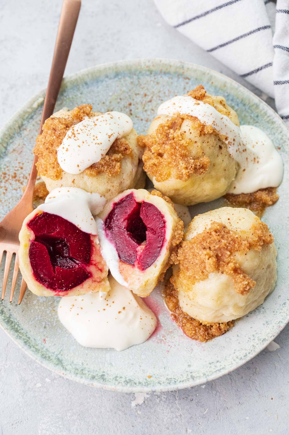 Polish plum dumplings (knedle ze śliwkami) served with sour cream and buttered breadcrumbs on a green plate.