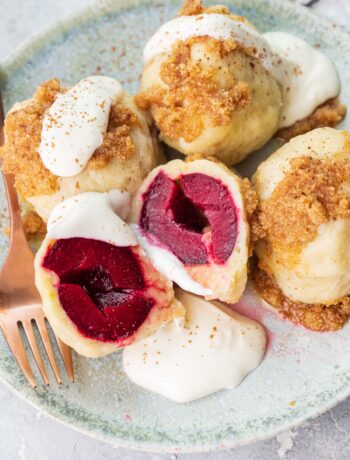 Polish plum dumplings (knedle ze śliwkami) served with sour cream and buttered breadcrumbs on a green plate.