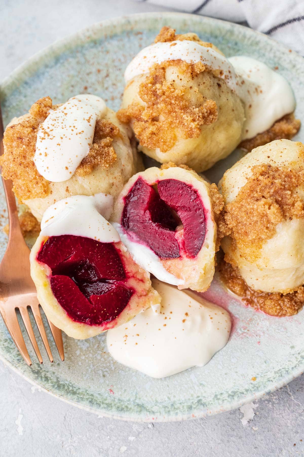 Polish plum dumplings (knedle ze śliwkami) served with sour cream and buttered breadcrumbs on a green plate.