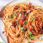 Pasta puttanesca on a white plate.