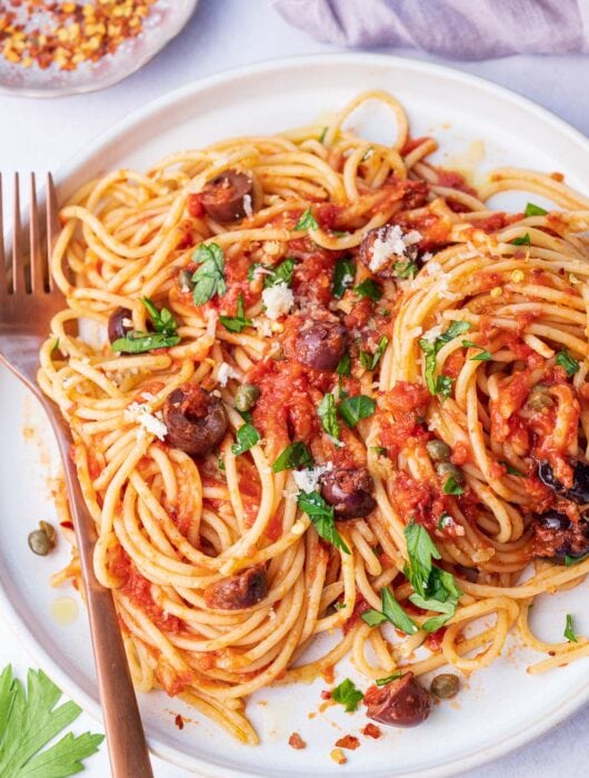 Pasta puttanesca on a white plate.