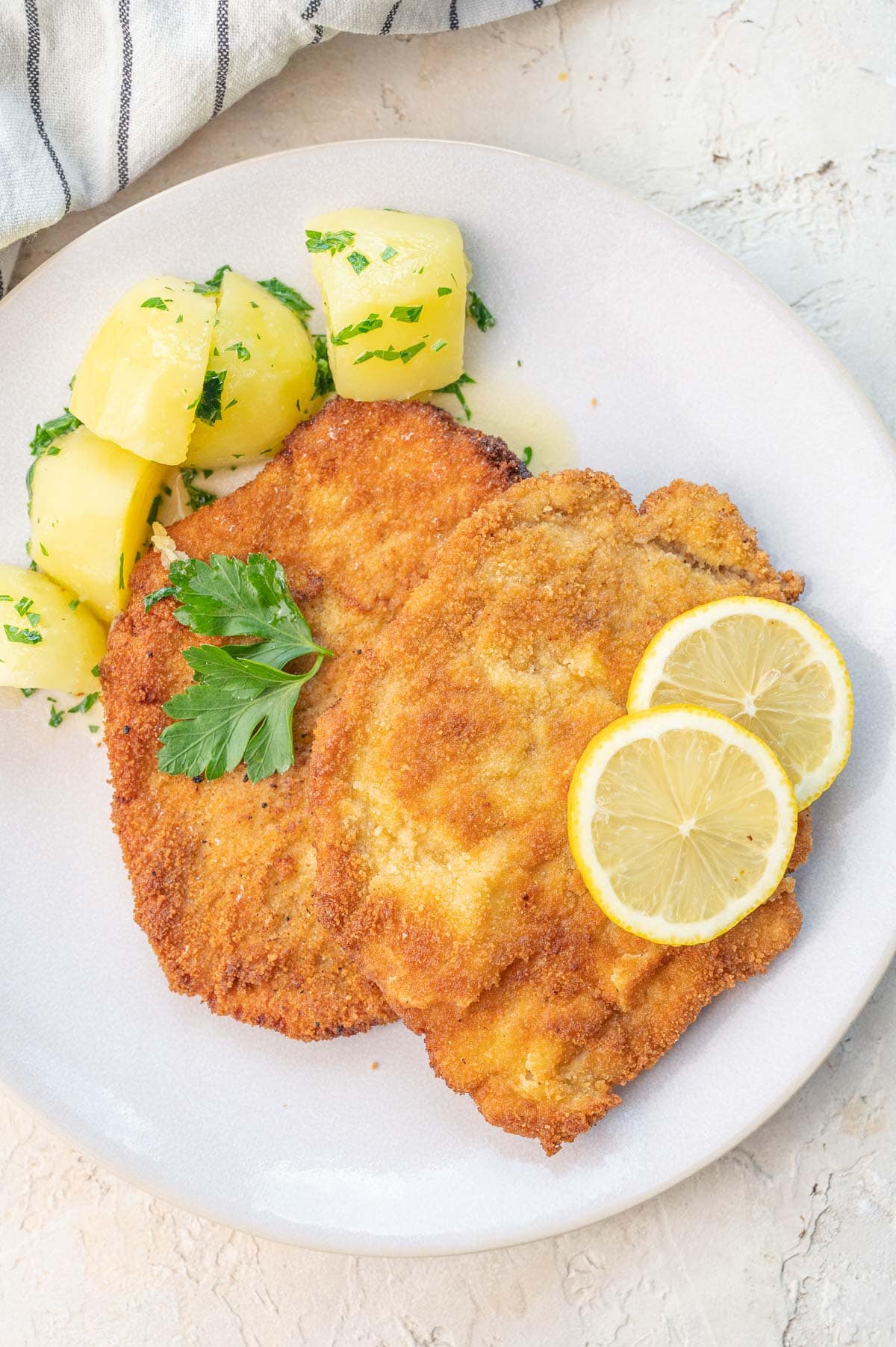 German pork schnitzel topped with lemon slices and served with potatoes on a beige plate.