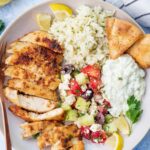 A bowl with Greek chicken, Greek salad, lemon rice, and tzatziki.
