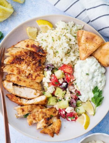 A bowl with Greek chicken, Greek salad, lemon rice, and tzatziki.