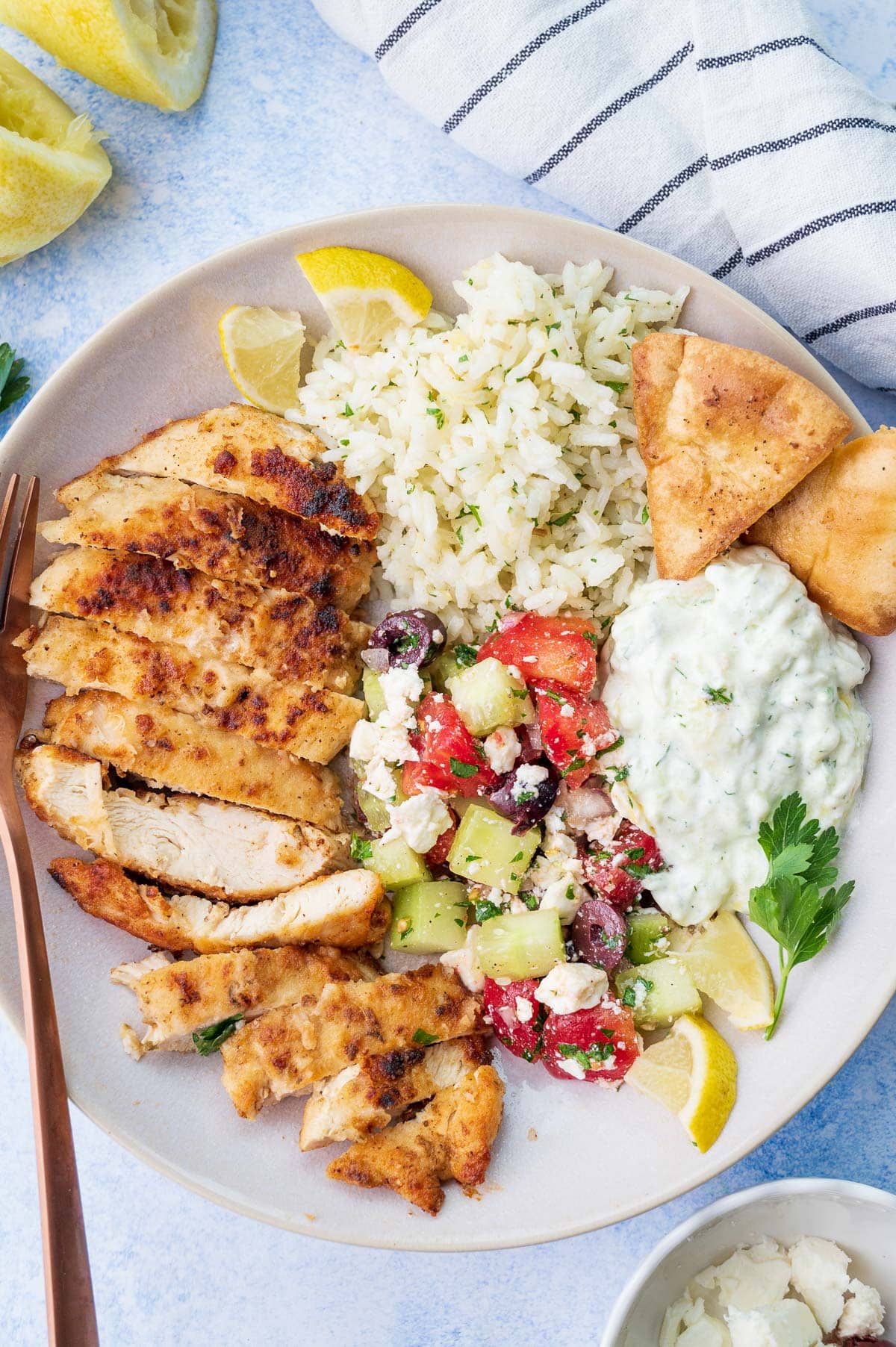 A bowl with Greek chicken, Greek salad, lemon rice and tzatziki.