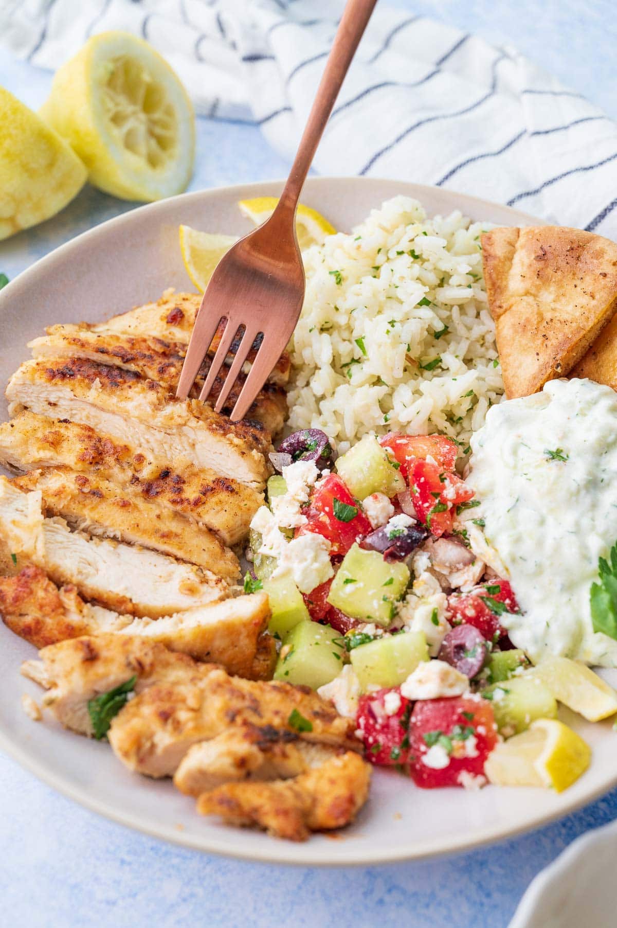 Greek chicken, Greek salad, lemon rice and tzatziki in a bowl. Chicken is being picked with a fork.