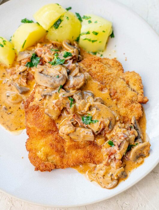 Jägerschnitzel with mushroom sauce served with potatoes on a beige plate.