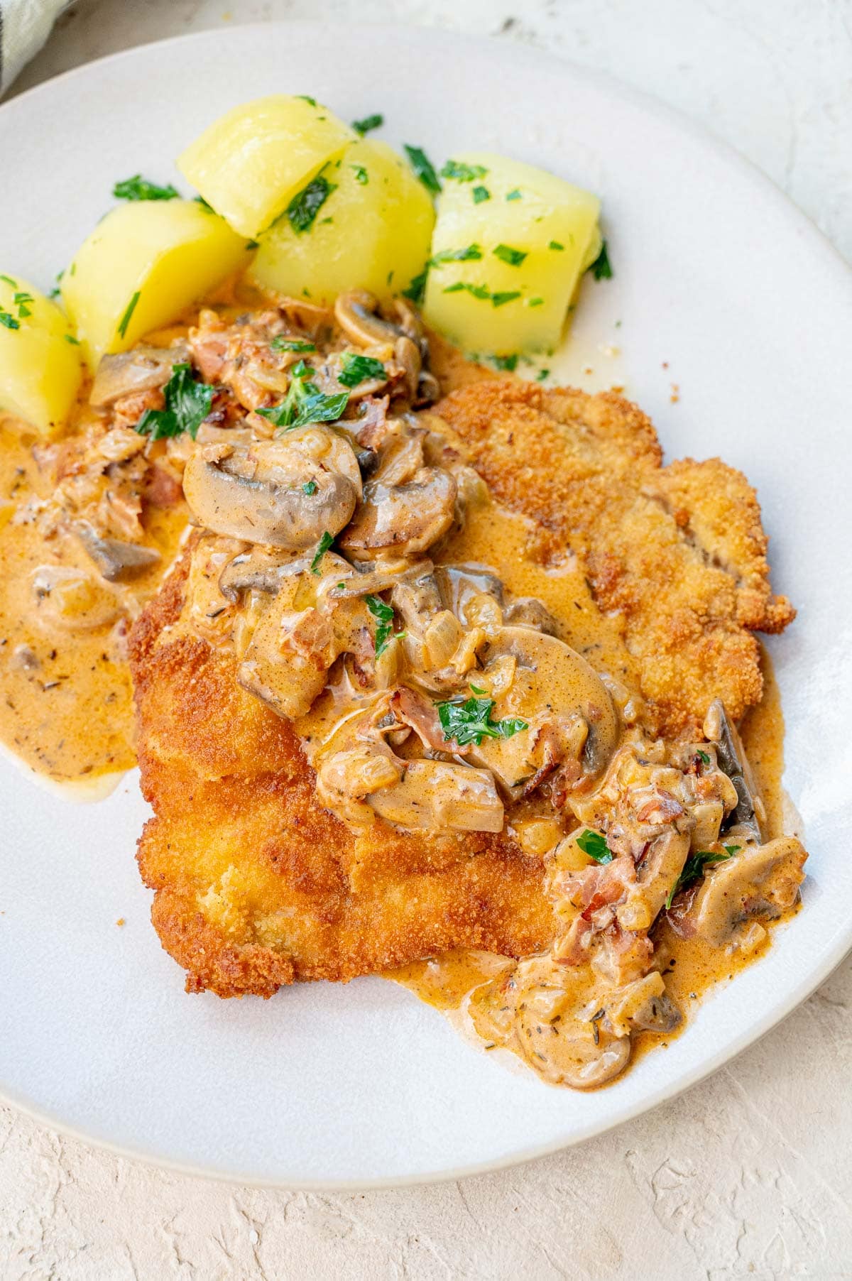 Jägerschnitzel with mushroom sauce served with potatoes on a beige plate.