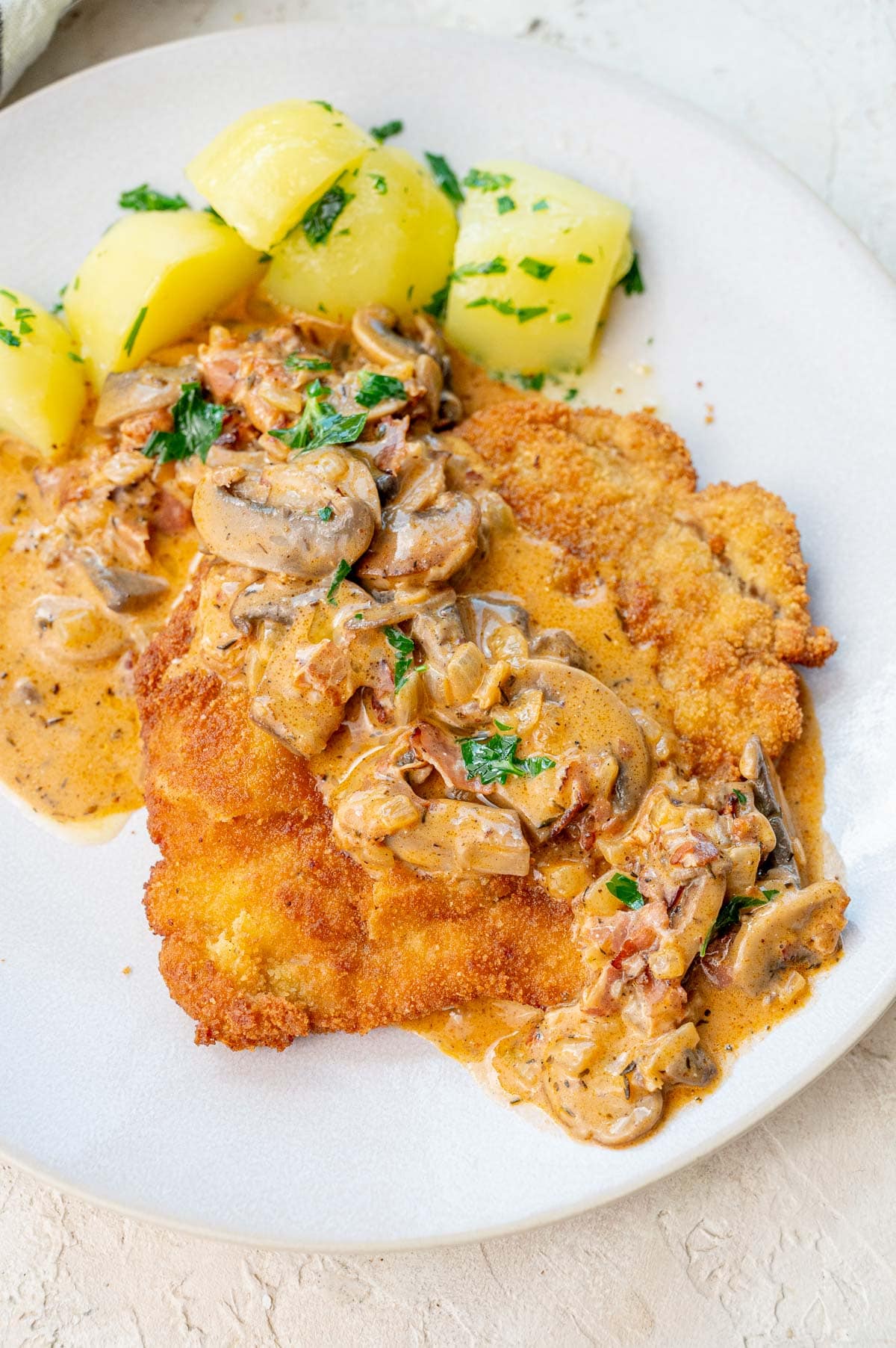 Jägerschnitzel with mushroom gravy and potatoes on a beige plate.