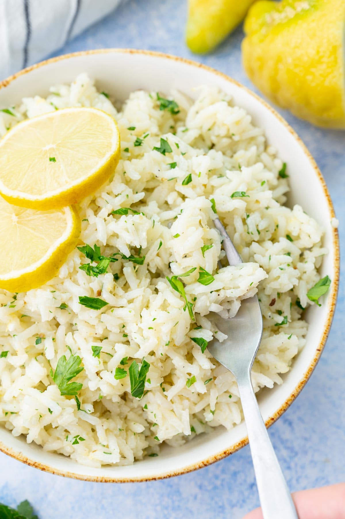 Lemon rice in a white bowl, topped with lemon slices and chopped parsley. A fork on the side.