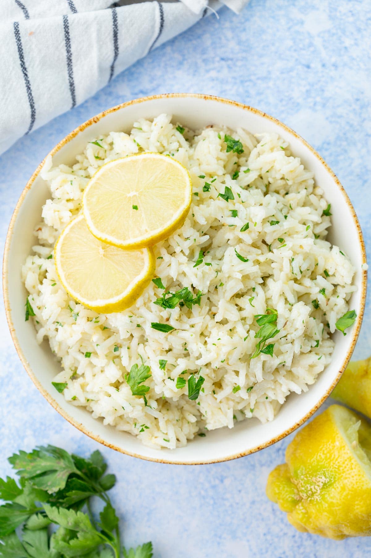 Lemon rice in a white bowl, topped with lemon slices and chopped parsley.