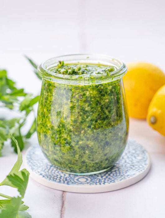 Parsley pesto in a jar. Parsley leaves and lemons in the background.