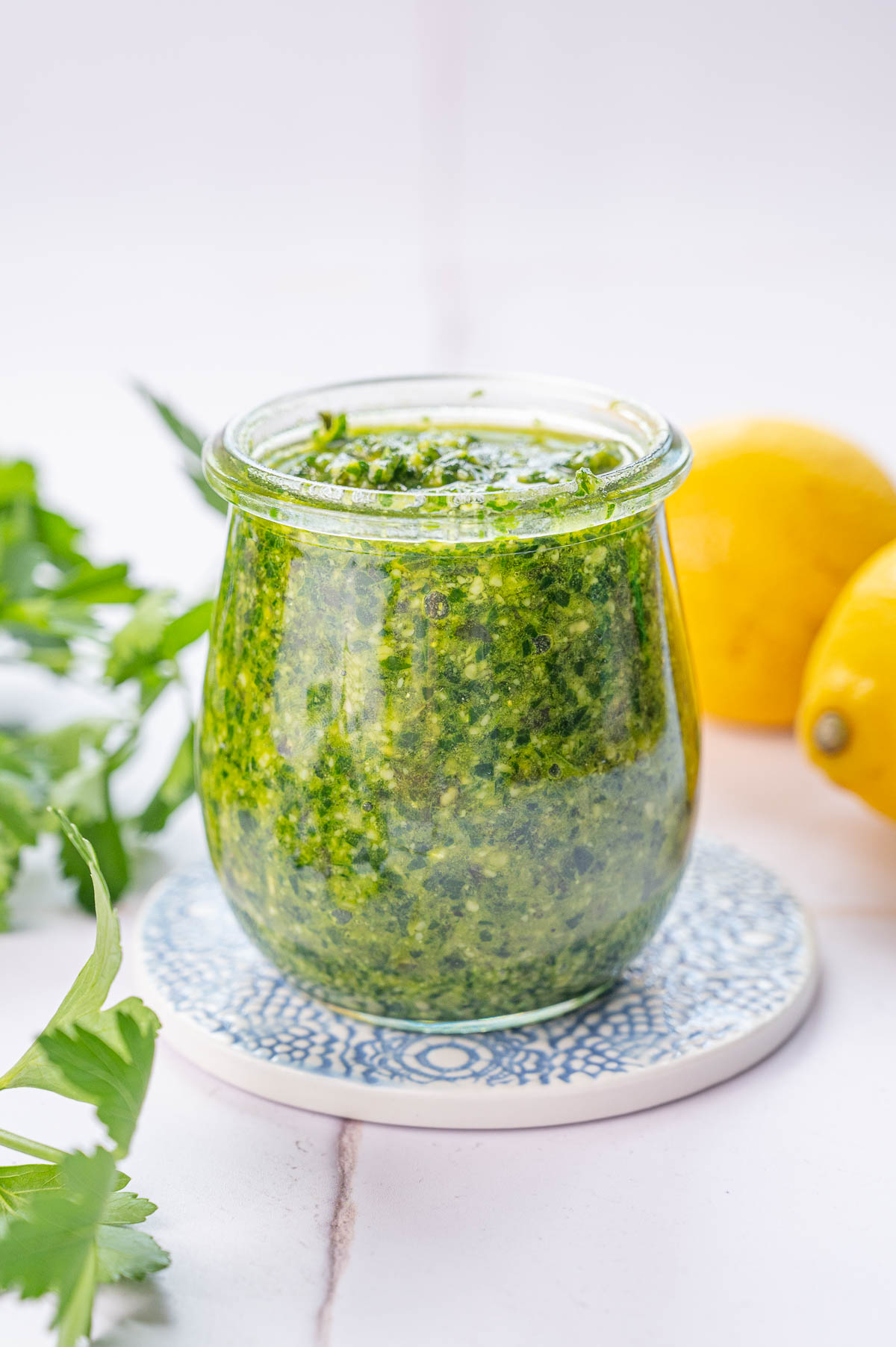 Parsley pesto in a jar. Parsley leaves and lemons in the background.