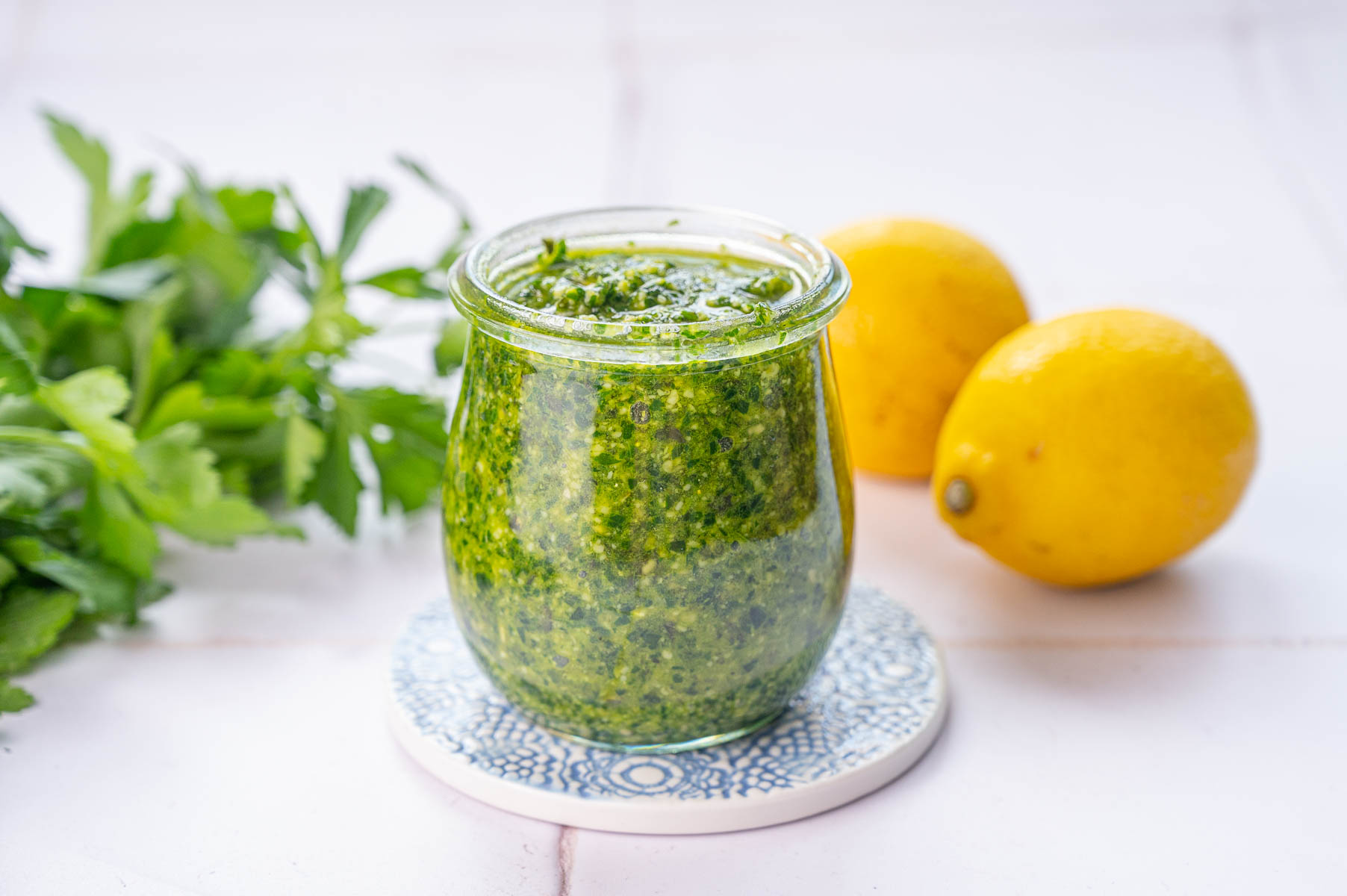 Parsley pesto in a jar. Parsley leaves and lemons in the background.