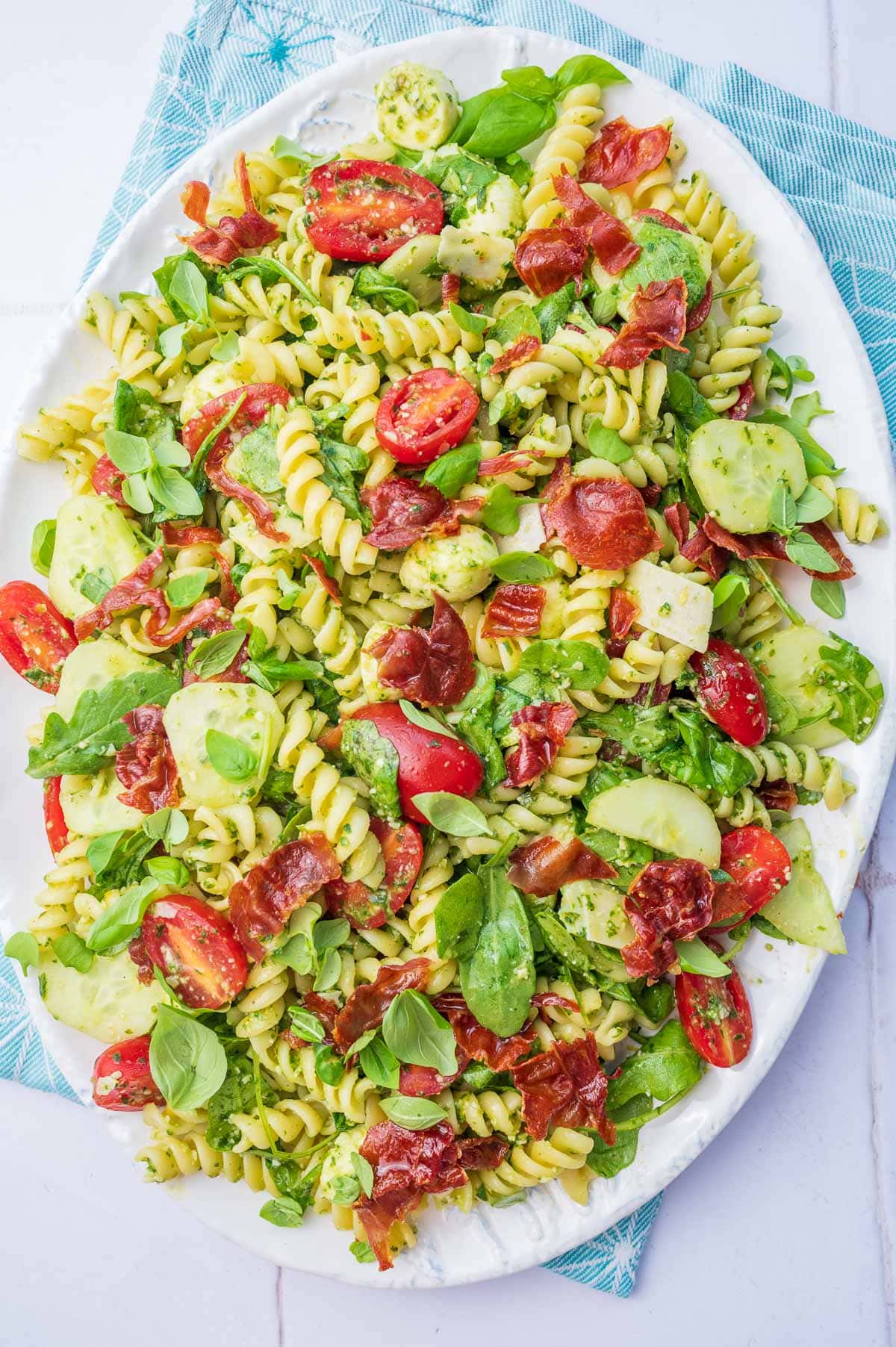 Pesto pasta salad on a white plate. Blue kitchen cloth in the background.