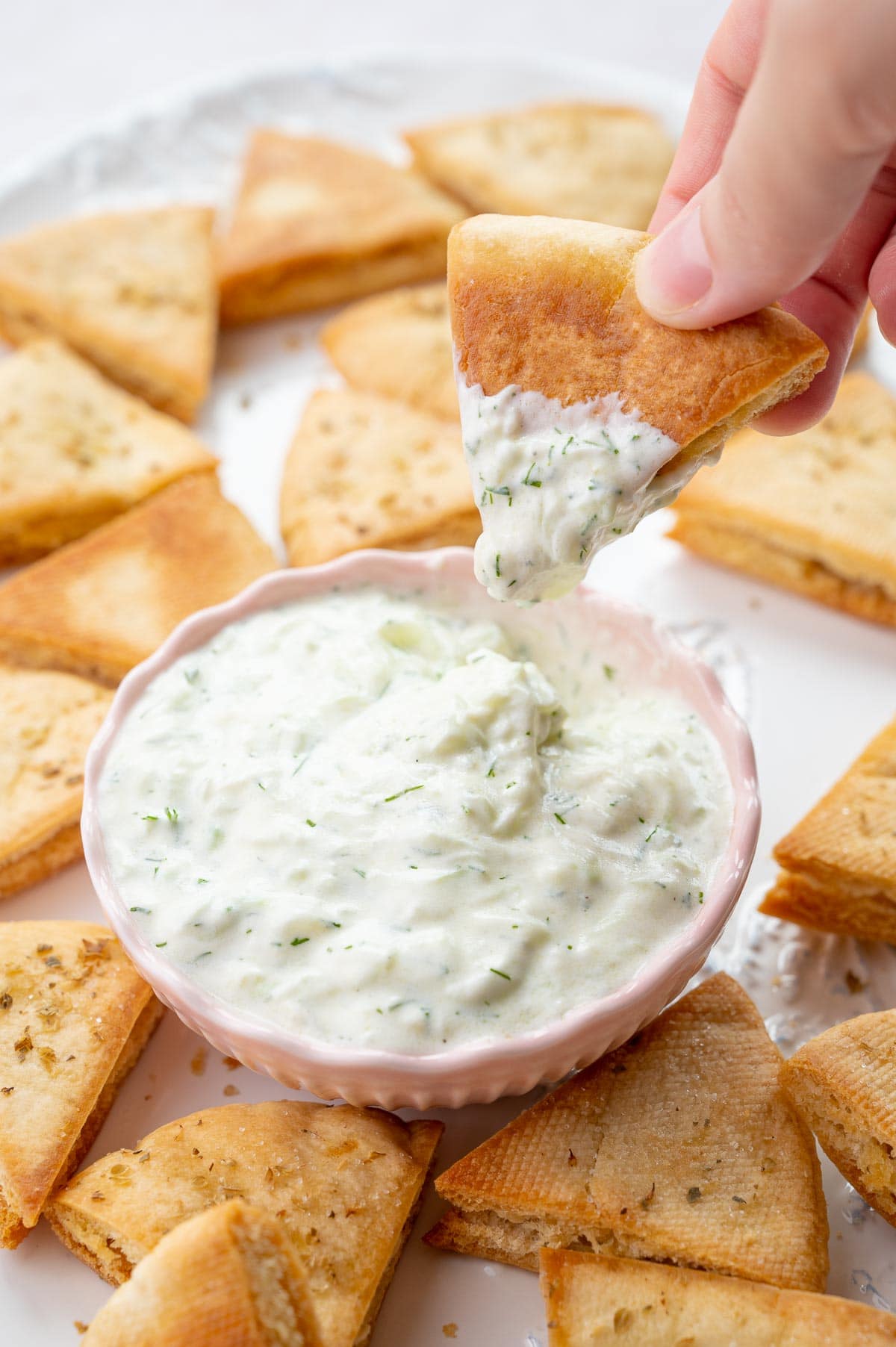 Tzatziki sauce is being scooped with a pita chip.