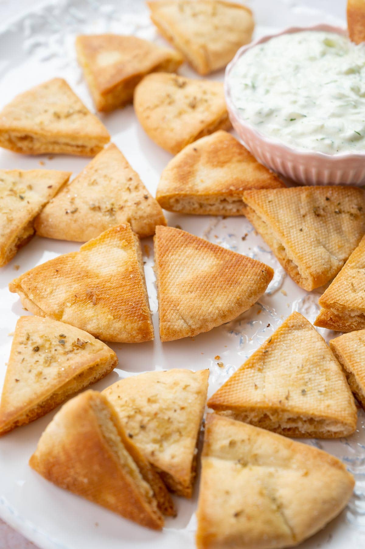 Pita chips on a white plate. Tzatziki sauce in a pink bowl.