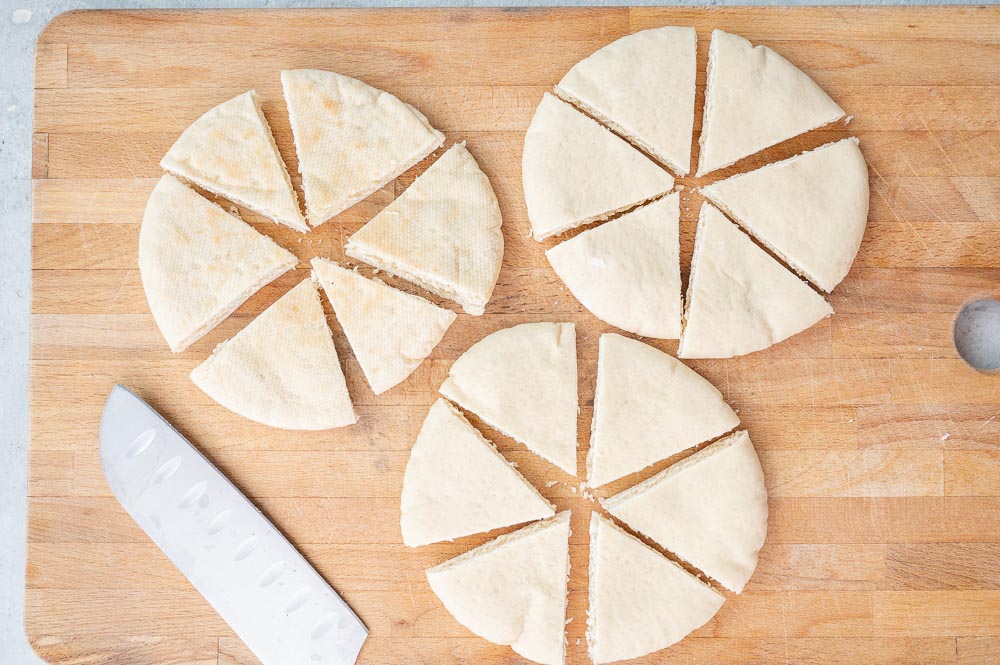 Pita breads cut into wedges on a wooden board.