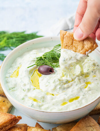 Tzatziki dip in a bowl is being scooped with a pita chip.