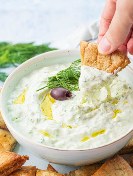 Tzatziki dip in a bowl is being scooped with a pita chip.