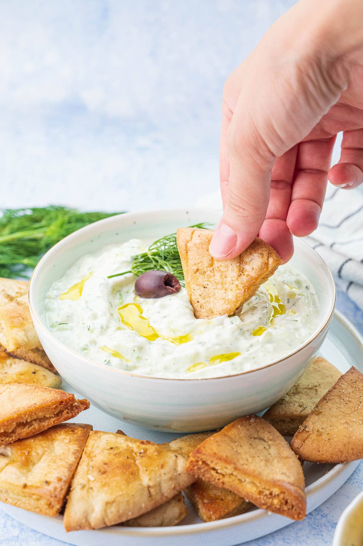 Tzatziki dip in a white bowl is being scooped with pita chips.