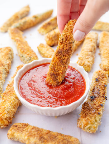 Zucchini fry is being dipped in marinara sauce.