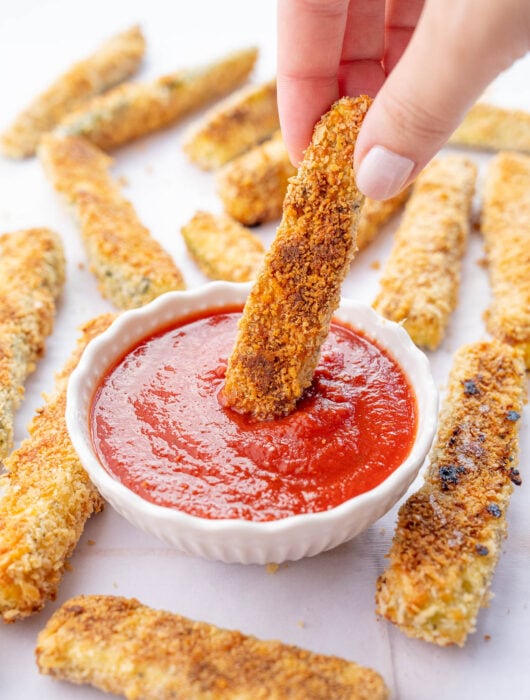 Zucchini fry is being dipped in marinara sauce.