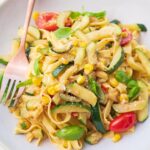 Zucchini pasta with corn and tomatoes on a beige plate.