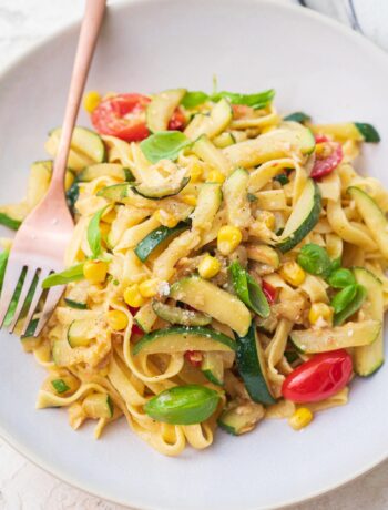 Zucchini pasta with corn and tomatoes on a beige plate.