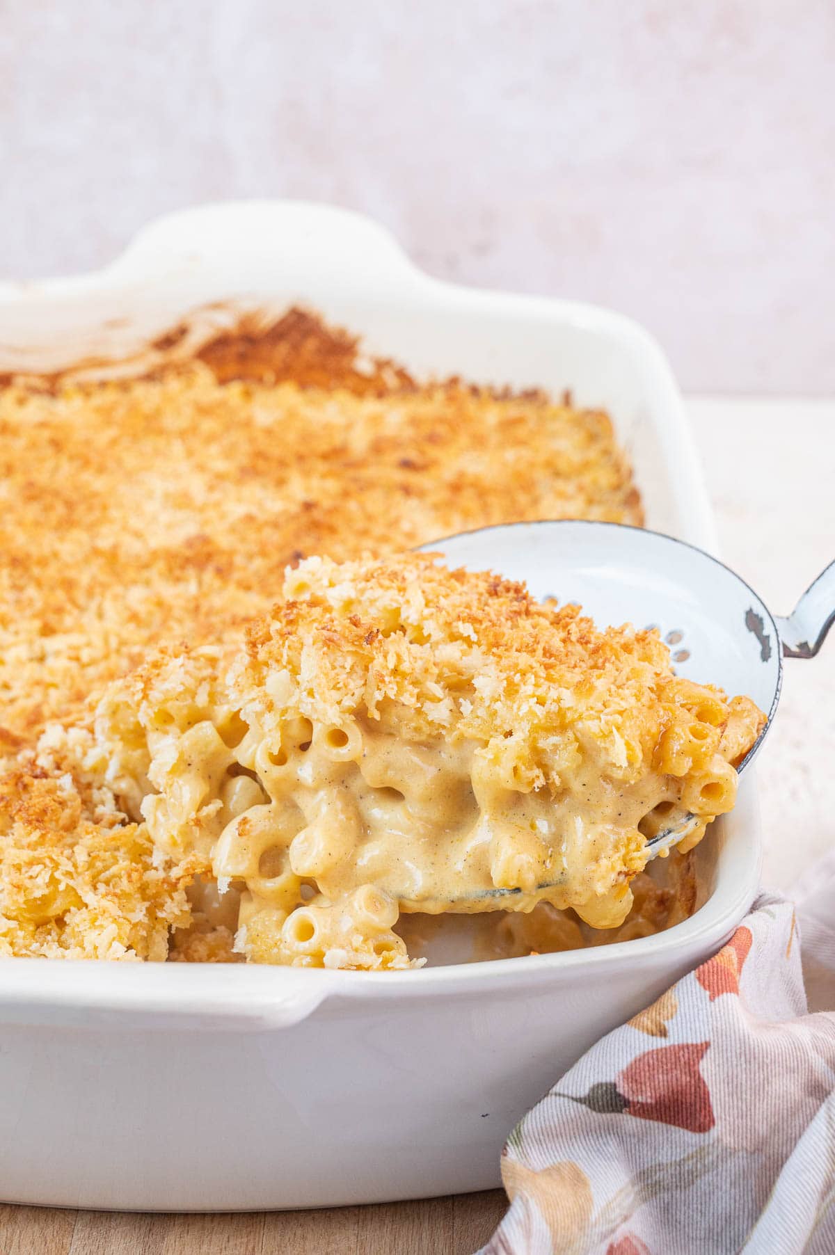 Gruyere mac and cheese on a slotted spoon being scooped out of a baking dish.