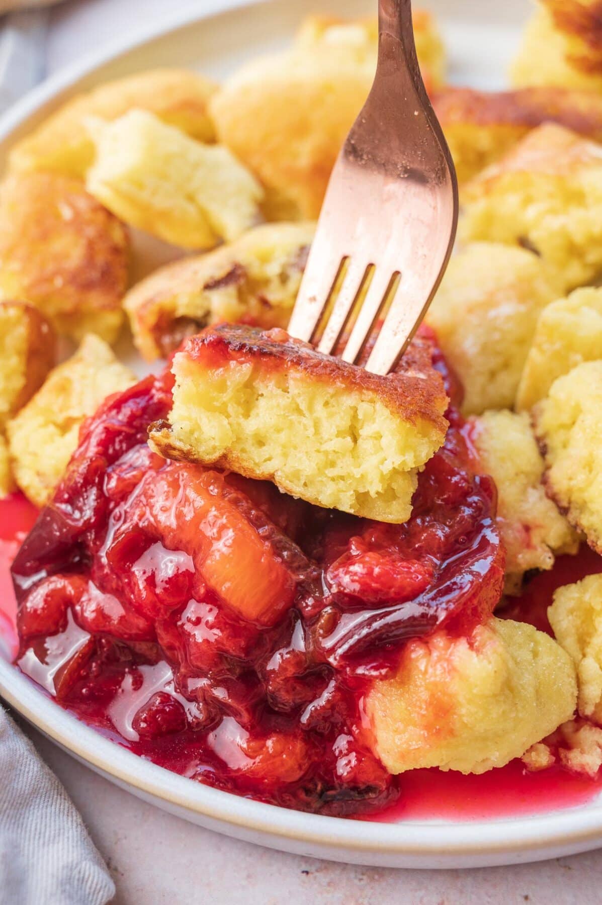 A piece of Kaiserschmarrn stuck on a fork is being dipped in plum compote.