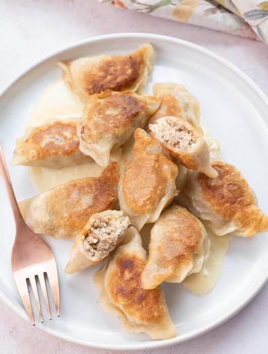 Meat pierogi with cheese sauce on a white plate.