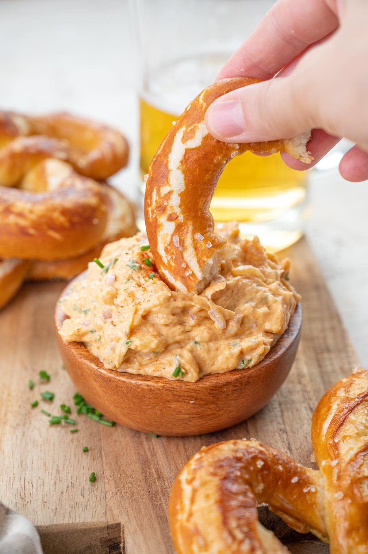 A piece of pretzel is being dipped in Obatzda dip.