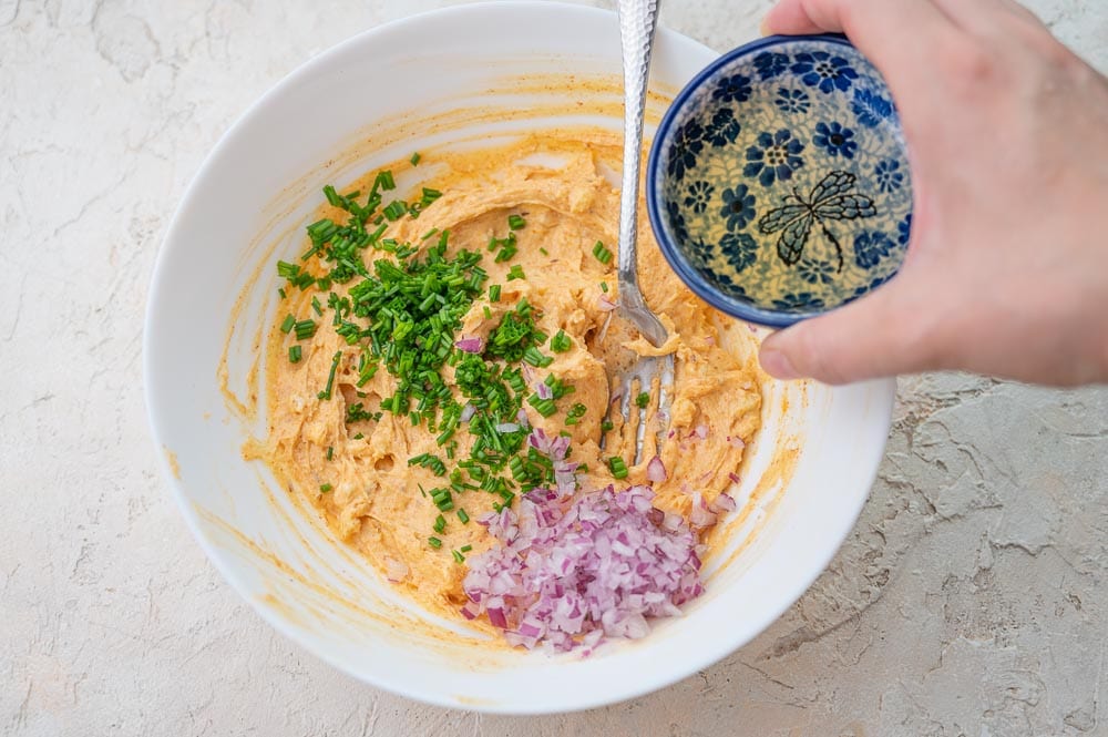 Beer is being added to Obatzda dip in a white bowl.