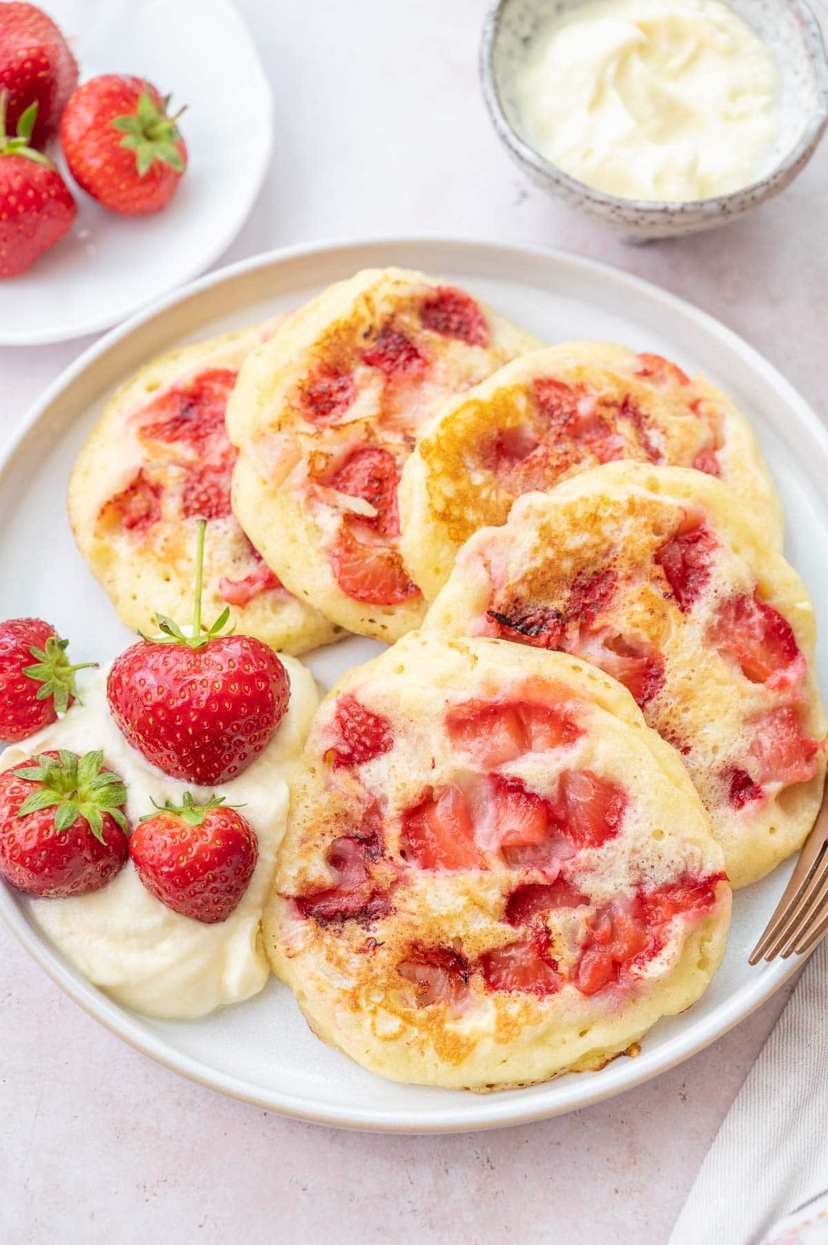 Strawberry pancakes served with whipped cream and strawberries on a white plate.