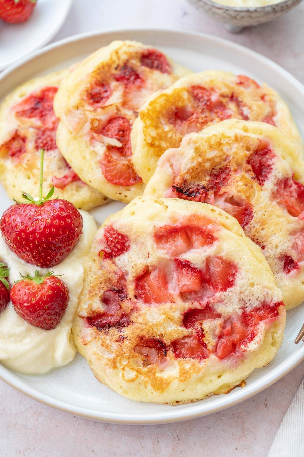 Strawberry pancakes served with whipped cream and strawberries on a white plate.