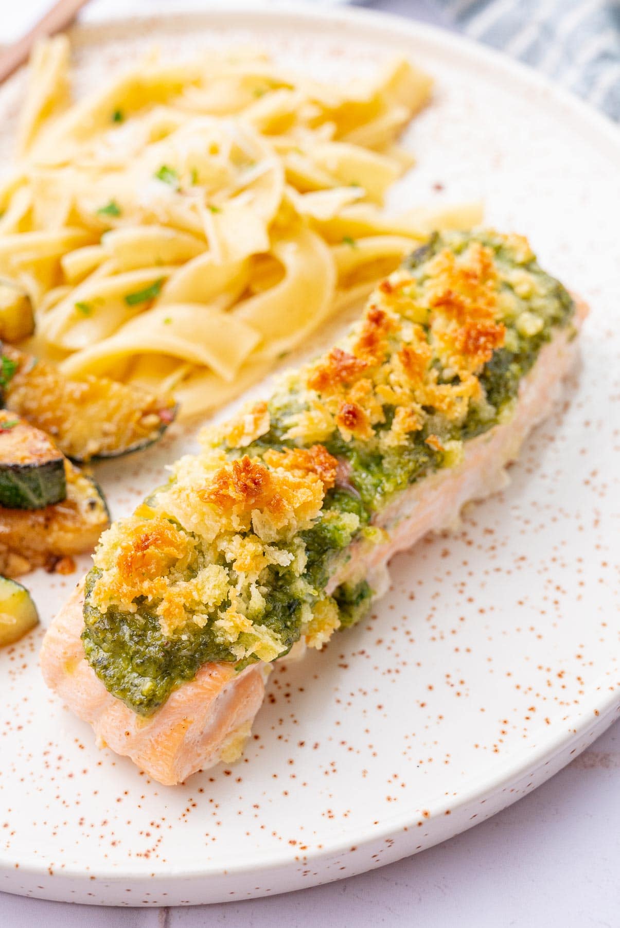 A close up photo of baked pesto salmon on a white plate.