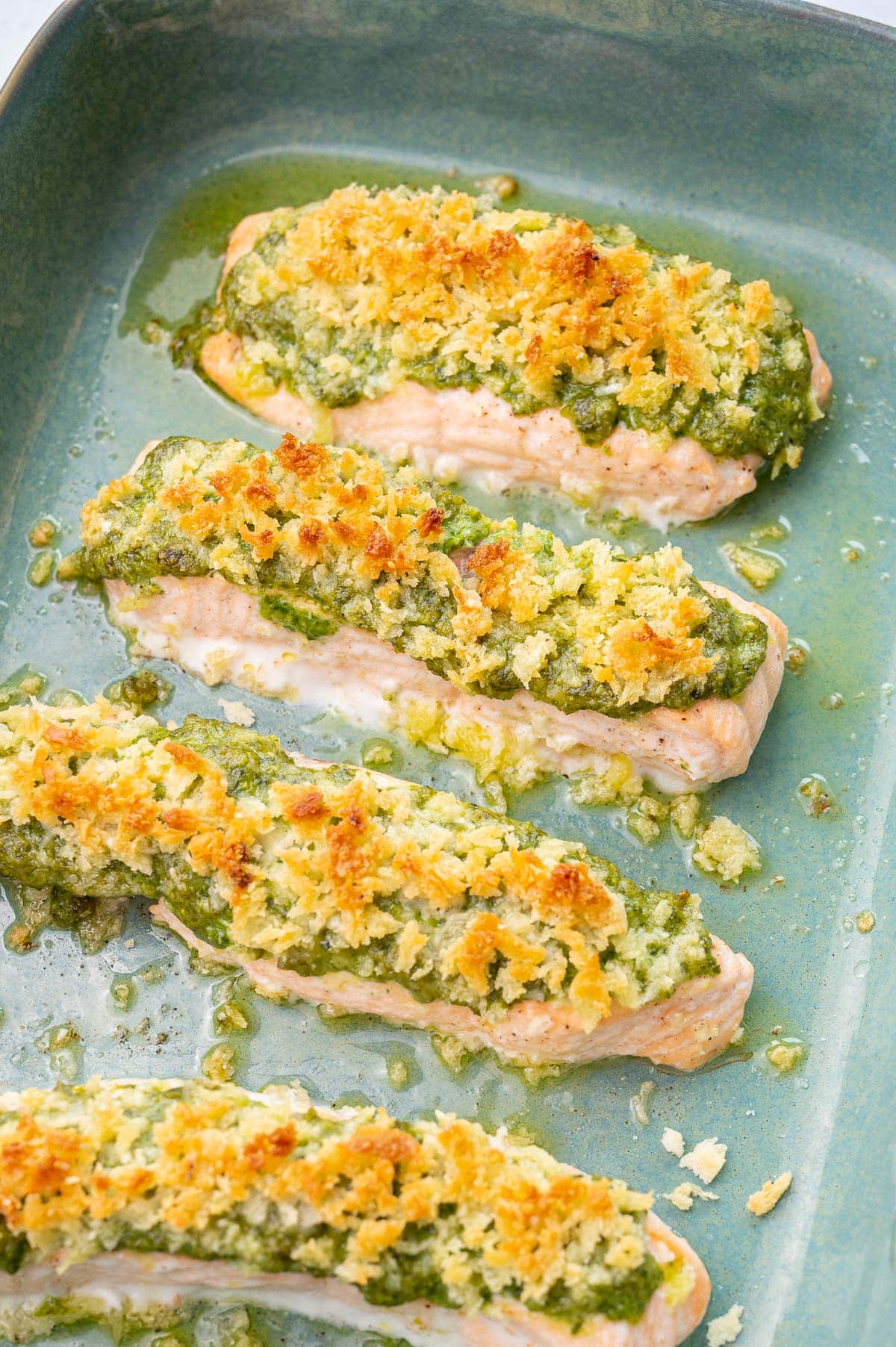 A close up photo of baked pesto salmon in a green baking dish.