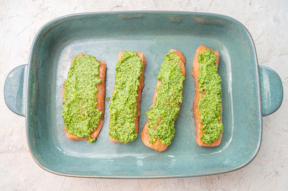 Salmon fillets topped with pesto in a green baking dish.