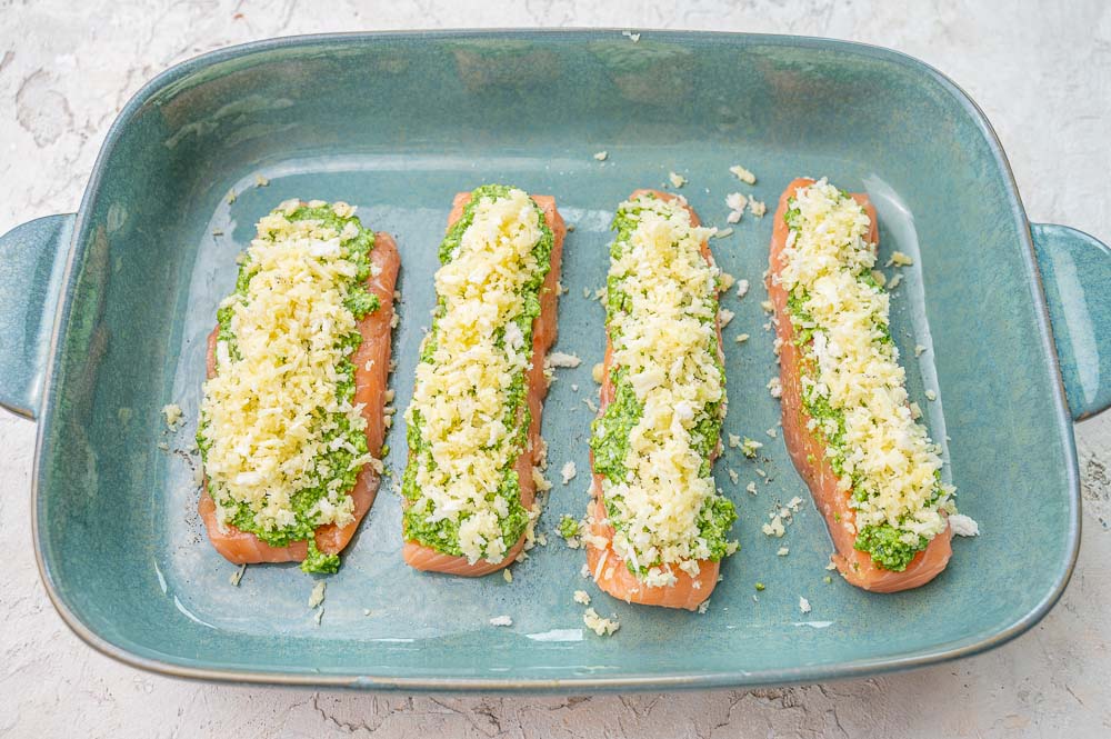 Salmon fillets topped with pesto and breadcrumb topping in a green baking dish.