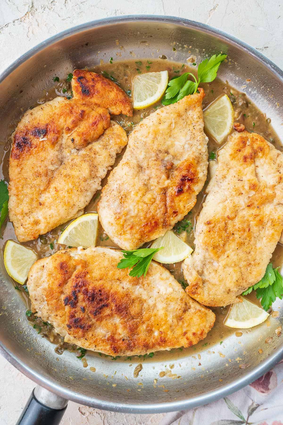 Pan-fried chicken breasts in piccata sauce in a frying pan.