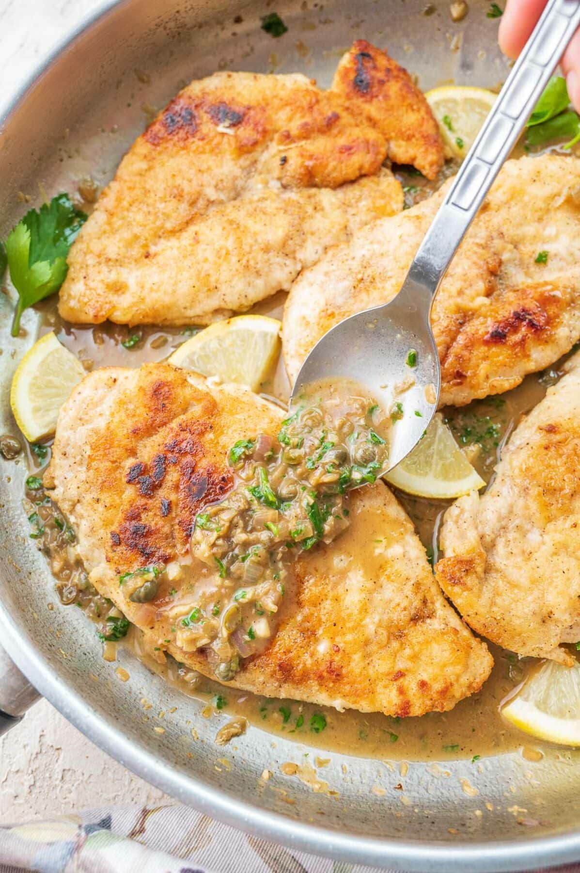 Pan-fried chicken piccata in a frying pan in poured with pan sauce.
