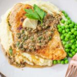 Chicken piccata served with mashed potatoes and peas on a plate.